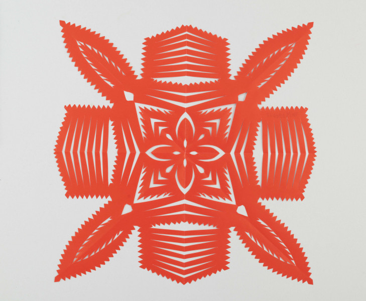 Wycinanka koloru czerwonego, przypominająca nałożone na siebie dwa krzyże; jeden o szerszych ramionach, drugi o ramionach płatkowych. Wokół wykończone ząbkami. W środku kompozycja z płatków i  strzałek, przypominająca kwiat. 