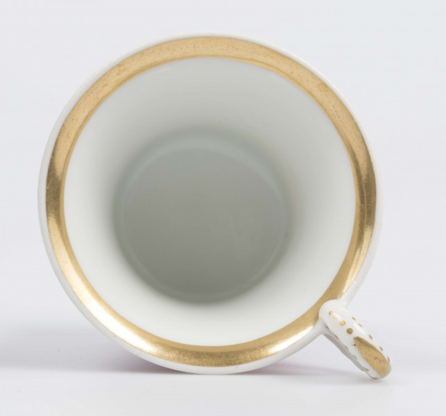 S/CS/133/1/ML - Filiżanka koniczna z rozchylonym wylewem, na niskiej stopie, ucho w formie pastorału z wolutą wyciągnietą ponad krawędź wylewu, zdobioną reliefową rozetką. Powierzchnia matowa malowana w całości na liliowy kolor, wylew obustronnie obwiedziony złotym paskiem, złotym konturem podkreślony brzeg stopy i profile ucha.
