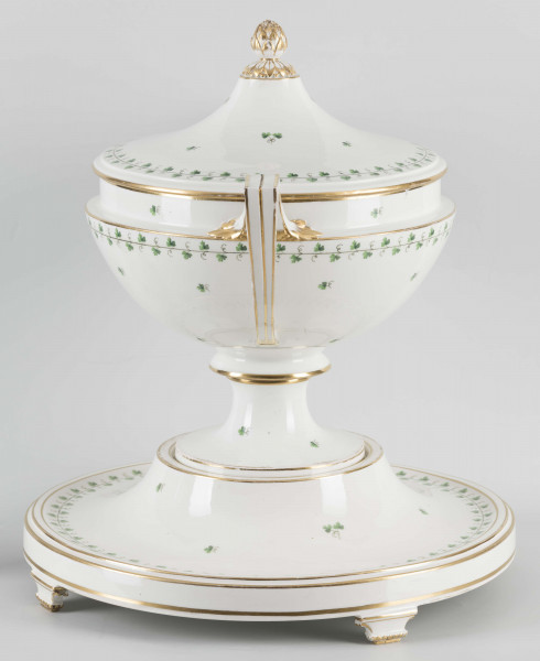 S/CS/1231/ML - Waza półkulista z przewężeniem poniżej wylewu, ucha łamane, stopa o okrągłej podstawie i wąskim trzonie wywiniętym u góry, pokrywa w formie wyniesionego stożka z plastycznym zwieńczeniem i uchwytem w kształcie szyszki. Dekoracja barwnie malowana i złocona: brzusiec, pokrywa i podstawa obwiedzione fryzem winorośli, na powierzchni rytmicznie rozrzucone pojedyncze liski, krawędzie, ucha i uchwyt pokrywy konturowane złotem, 
Podstawa w formie wyniesionego ściętego stożka z okrągłym wgłębieniem u góry, na trzech kostkowych nóżkach. 
 
