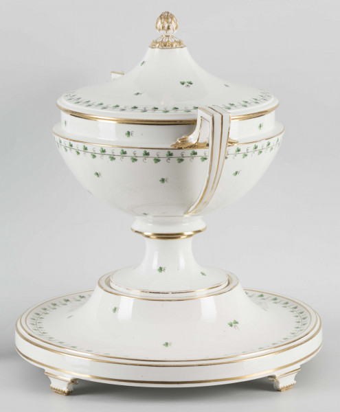 S/CS/1231/ML - Waza półkulista z przewężeniem poniżej wylewu, ucha łamane, stopa o okrągłej podstawie i wąskim trzonie wywiniętym u góry, pokrywa w formie wyniesionego stożka z plastycznym zwieńczeniem i uchwytem w kształcie szyszki. Dekoracja barwnie malowana i złocona: brzusiec, pokrywa i podstawa obwiedzione fryzem winorośli, na powierzchni rytmicznie rozrzucone pojedyncze liski, krawędzie, ucha i uchwyt pokrywy konturowane złotem, 
Podstawa w formie wyniesionego ściętego stożka z okrągłym wgłębieniem u góry, na trzech kostkowych nóżkach. 
 
