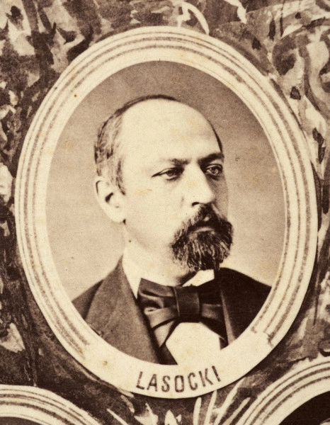 Fotografie w odcieniu sepii umieszczone na tle drzew i roślin, w centralnym miejscu postać kobiety ze sztandarem i aniołkami, wkomponowane widoki budowanej stacji, mostu kolejowego i lokomotywy. Największe zdjęcie w górnej, środkowej części bez podpisu, prawdopodobnie inż. głównej kolei nadwiślańskiej Tadeusz Chrzanowski lub jego następca Walery Titkow. Wśród podobizn pracownicy Biura Głównego Inżyniera: inż. Włodzimierz Stanisławski - pomocnik głównego inżyniera; inż. Feliks Kucharzewski -  pomocnik naczelnika biura; Feliks Kamocki - naczelnik kancelarii; Witold Lanci - naczelnik Wydz. Architektury; dr Wacław Lasocki- służba zdrowia; Władysław Radwan - sprawy zakupu gruntów; inż. Stanisław hr Scipio - projektant mostów kolejowych i jego współpracownicy: inż. Stefan Zieliński, inż. Maurycy Machalski, inż. Feliks Kucharzewski. Fotografia w passe - partout, za szkłem, oprawiona w drewnianą, profilowaną ramę.