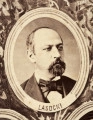 Fotografie w odcieniu sepii umieszczone na tle drzew i roślin, w centralnym miejscu postać kobiety ze sztandarem i aniołkami, wkomponowane widoki budowanej stacji, mostu kolejowego i lokomotywy. Największe zdjęcie w górnej, środkowej części bez podpisu, prawdopodobnie inż. głównej kolei nadwiślańskiej Tadeusz Chrzanowski lub jego następca Walery Titkow. Wśród podobizn pracownicy Biura Głównego Inżyniera: inż. Włodzimierz Stanisławski - pomocnik głównego inżyniera; inż. Feliks Kucharzewski -  pomocnik naczelnika biura; Feliks Kamocki - naczelnik kancelarii; Witold Lanci - naczelnik Wydz. Architektury; dr Wacław Lasocki- służba zdrowia; Władysław Radwan - sprawy zakupu gruntów; inż. Stanisław hr Scipio - projektant mostów kolejowych i jego współpracownicy: inż. Stefan Zieliński, inż. Maurycy Machalski, inż. Feliks Kucharzewski. Fotografia w passe - partout, za szkłem, oprawiona w drewnianą, profilowaną ramę.