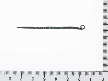 1562/A/ML - Szpila brązowa z drutu o przekroju okrągłym. Główka rozklepana i zawinięta w uszko. Surowiec - brąz. Sposób wykonania - kucie. Stan zachowania - dobry. 