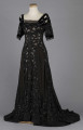 S/T/243/ML - Suknia wizytowa, czarna, uszyta z atłasu jedwabnego, jedwabnego tiulu i aksamitu, haftowana cekinami. Krótki rękaw z jedwabnego czarnego aksamitu, dekolt prostokatny, dość głęboki, wykończony wstawką haftowaną i aksamitem. Kolory są kontrastowe. Spodnia warstwa sukni, z białej tafty i muślinu, widoczna w partiach sukni szytych z czarnego tiulu, dodaje całości elegancji. Brzegi dekoracyjnej wici z tafty zaakcentowane naszytymi cekinami. Suknia do ziemi z tyłu krótki tren. Brak halki. 
