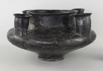 598/A/ML 598/A/ML - naczynie kultowe (kernos) kultury pomorskiej;
wymiary dodatkowe: 25,0 cm - średnica centralnego wylewu
opis: naczynie wazowate o czarnej, błyszczącej powierzchni, którego brzusiec został ozdobiony ornamentem złożonym z linii rytych oraz nakłuć; wokół głównego otworu posiada cztery symetrycznie rozmieszczone kielichy-rytony, które mają nieco wydęte ścianki boczne i kielichowato rozchylone na zewnątrz krawędzie otworów; rytony łączą się z głównym otworem kanalikami;