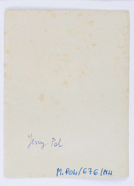 Fotografia przedstawia Jerzego Pola, siedzącego na beczce, z opartymi na kolanach rękoma. Mężczyzna w średnim wieku, ubrany w białą koszulę, ciemne spodnie wpuszczone w zawiązywane trzewiki. W tle widoczne liczne krzewy i drzewa. Fotografia obwiedziona białą ramką.