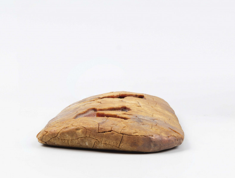 Zawieszka bursztynowa trapezowata z zaokrąglonymi kątami, płasko-wypukła w przekroju poprzecznym, przy węższym boku 2 koliste otwory przewiercone z dwóch stron. 