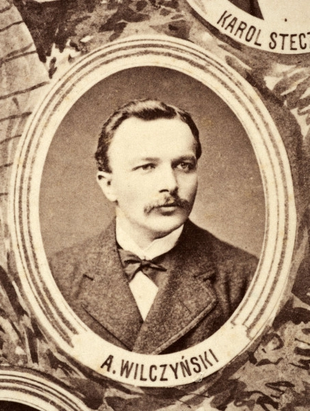 Fotografie w odcieniu sepii umieszczone na tle drzew i roślin, w centralnym miejscu postać kobiety ze sztandarem i aniołkami, wkomponowane widoki budowanej stacji, mostu kolejowego i lokomotywy. Największe zdjęcie w górnej, środkowej części bez podpisu, prawdopodobnie inż. głównej kolei nadwiślańskiej Tadeusz Chrzanowski lub jego następca Walery Titkow. Wśród podobizn pracownicy Biura Głównego Inżyniera: inż. Włodzimierz Stanisławski - pomocnik głównego inżyniera; inż. Feliks Kucharzewski -  pomocnik naczelnika biura; Feliks Kamocki - naczelnik kancelarii; Witold Lanci - naczelnik Wydz. Architektury; dr Wacław Lasocki- służba zdrowia; Władysław Radwan - sprawy zakupu gruntów; inż. Stanisław hr Scipio - projektant mostów kolejowych i jego współpracownicy: inż. Stefan Zieliński, inż. Maurycy Machalski, inż. Feliks Kucharzewski. Fotografia w passe - partout, za szkłem, oprawiona w drewnianą, profilowaną ramę.
