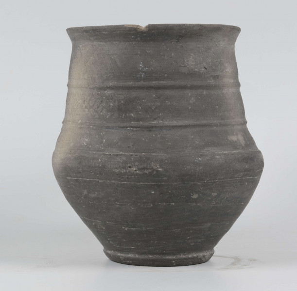 Dno płaskie, wyraźnie wyodrębnione stopką skośnie ściętą ku dołowi; dno wyodrębnione od części przydennej dookolnym wgłębieniem; lekko rozszerzające się ku górze, brzusiec łagodnie zaokraglony, ku górze zwężający się, przechodzący w wysoką, cylindryczną szyjkę; wylew płasko ścięty, rozchylony na zewnątrz; na największej wydętości brzuśca dookolny żłobek; w miejscu przejścia brzuśca w szyję i w połowie szyi dookolny wypukłe listwy; ucho z taśmy środkiem wklęsłej, biegnące od wylewu do załomu brzuśca, szyja zdobiona różnym ornamentem (trzy pasy) przez wygładzenie; powierzchnia gładzona, wyświecona
wymiary dodatkowe: 17,0 cm (obwód); 8,0 cm (śr. dna); 0,3 cm (wys. stopki); 0,5 cm (wys. szyi)