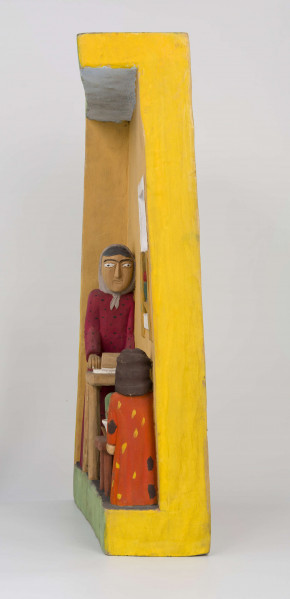 Płaskorzeźba w drewnie lipowym, polichromowana, przedstawiająca wnętrze kuchni, wykonana w jednym kawału drewna. Wnętrze kuchni zaznaczone z lewej strony występem szer. 6,7 cm i gł. 4,5 cm. U góry podkreślony „sufit” wys. 3 cm i gł. 5 cm. Na postumencie wys. 3,5 cm i gł. 4,5 cm. Z lewej strony zakomponowana postać kobiety (z profilu). Kobieta stoi lekko pochylona nad stołem, na którym wałkuje ciasto. Ubrana jest w długą czerwoną suknię w czarne kropki, z długim rękawem.  Na głowie ma zawiązaną, pod brodą, popielatą chustkę, spod której wystają czarne włosy. Twarz płaska, oczy lekko wypukłe, brwi czarne łukowate, nos długi prosty. 
Pod stołem stoi dzbanek, którego brzusiec ozdobiony jest czteropłatkowym kwiatem. Płatki w kolorze czerwony, środek zielony. Wylew podkreślony zielonym paskiem. Z prawej strony przy niskim brązowym stołku, po obu stronach stoją dzieci, które z jednej miski jedzą obiad. Z lewej strony stołka postać chłopca (wys. 12,5 cm) w szarych spodniach, sięgających za kolana i w zielonej koszuli wypuszczonej na spodnie. Twarz chłopca płaska, włosy czarne sięgające do ramion. W prawej ręce chłopiec trzyma łyżkę.  Z prawej – dziewczynka (wys. 13,6 cm), w długiej czerwonej sukience w żółto-czarne ciapki. Włosy czarne, sięgające ramion, twarz płaska. W prawej ręce trzyma łyżkę zanurzoną w misce, lewa opuszczona swobodnie. 
Na wys. 15,5 cm, z prawej strony, okno z kwiatami na parapecie i zasłonkami po bokach, do połowy okna. Wym. okna: wys. 14,5 cm, szer. 11,6 cm.