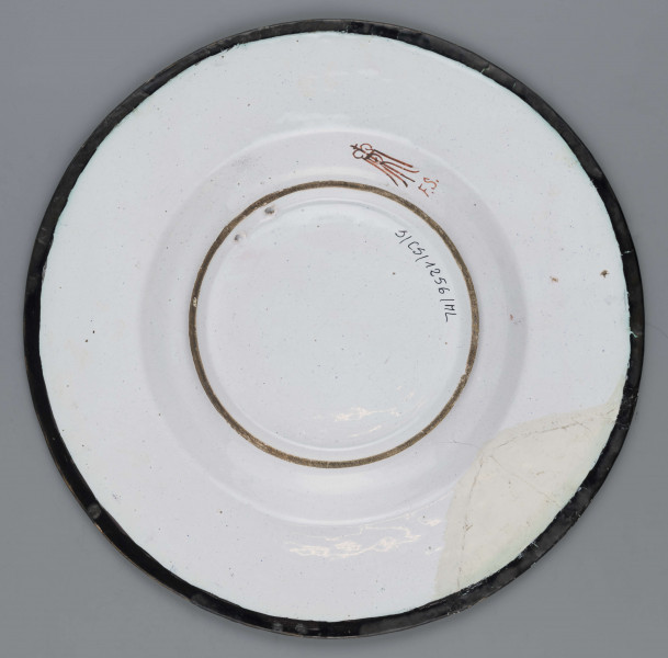 S/CS/1256/ML - Talerz okrągły, gładki, szkliwiony, dekoracja malowana wielobarwnie. W lustrze malowane przedstawienie księcia Józefa Poniatowskiego na koniu na tle uproszczonego pejzażu.  
Książę w mundurze ułańskim, z burka na ramionach, dosiada karego konia. Kołnierz pokryty fryzem akantowych wolut malowanych czarno na żółtym tle, przerwanym na osi u góry i u dołu dwoma kartuszami herbowymi: w górnym Orzeł, w dolnym Pogoń.