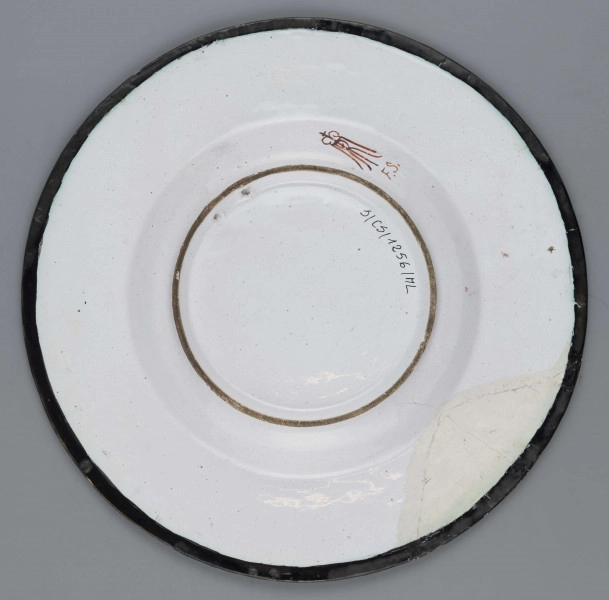 S/CS/1256/ML - Talerz okrągły, gładki, szkliwiony, dekoracja malowana wielobarwnie. W lustrze malowane przedstawienie księcia Józefa Poniatowskiego na koniu na tle uproszczonego pejzażu.  
Książę w mundurze ułańskim, z burka na ramionach, dosiada karego konia. Kołnierz pokryty fryzem akantowych wolut malowanych czarno na żółtym tle, przerwanym na osi u góry i u dołu dwoma kartuszami herbowymi: w górnym Orzeł, w dolnym Pogoń.