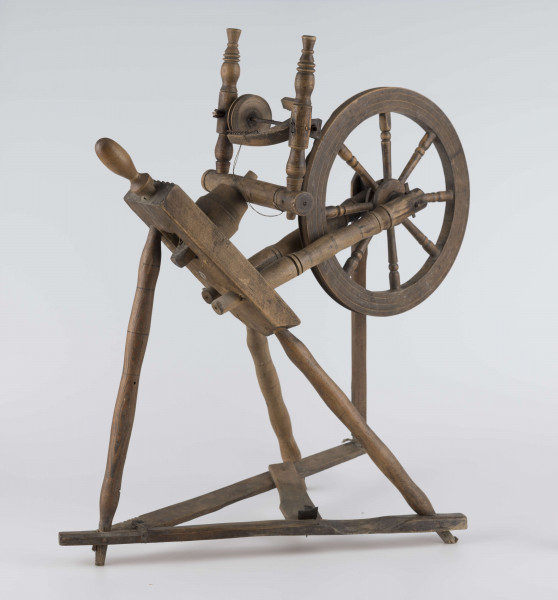 E/16647/ML - Kołowrotek poziomy, drewniany, ozdobnie toczony. Drewno niemalowane. Podstawa to 3 skośnie ustawione nóżki. Dwie z nich osadzone w wąskiej listwie. Górne końce nóżek osadzone w prostokątnej pochyłej grubej desce (11 x 32 x 4 cm). Stanowi ona podstawę do osadzenia koła napędowego i szpuli zwijającej nici. W niej zamocowany uchwyt połączony ze śrubą, która reguluje położenie szpuli. Koło osadzone na metalowej ośce posiada 8 toczonych ozdobnie szprych. Jeden koniec ośki połączony pionową ruchomą listewką z pedałem wprawiającym w ruch kołowrotek. Szpula osadzona również na metalowej ośce.