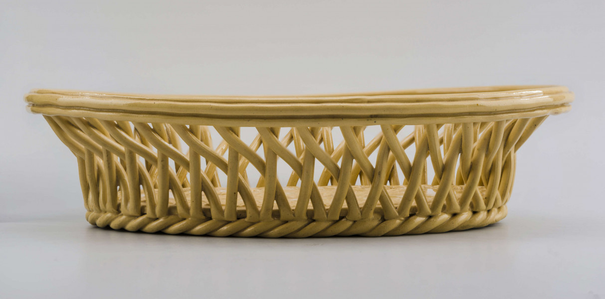 Koszyczek owalny głęboki; dno pełne od zewnątrz obwiedzione warkoczem, boki z okrągłych wałków przeplecionych ukośnie, połączonych profilowaną obręczą tworzącą krawędź. W lustrze (na dnie) dekoracja reliefowa: pośrodku bukiet kwiatów w wazonie, wokół brzegu wić laurowa z owocami. Całość pokryta połyskliwą glazurą w kolorze jasnego ugru.
 