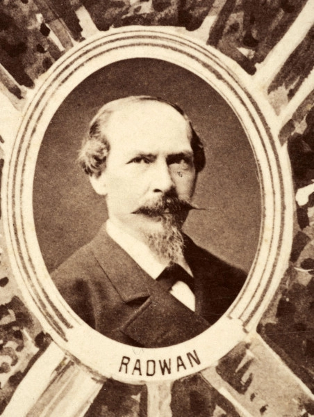 Fotografie w odcieniu sepii umieszczone na tle drzew i roślin, w centralnym miejscu postać kobiety ze sztandarem i aniołkami, wkomponowane widoki budowanej stacji, mostu kolejowego i lokomotywy. Największe zdjęcie w górnej, środkowej części bez podpisu, prawdopodobnie inż. głównej kolei nadwiślańskiej Tadeusz Chrzanowski lub jego następca Walery Titkow. Wśród podobizn pracownicy Biura Głównego Inżyniera: inż. Włodzimierz Stanisławski - pomocnik głównego inżyniera; inż. Feliks Kucharzewski -  pomocnik naczelnika biura; Feliks Kamocki - naczelnik kancelarii; Witold Lanci - naczelnik Wydz. Architektury; dr Wacław Lasocki- służba zdrowia; Władysław Radwan - sprawy zakupu gruntów; inż. Stanisław hr Scipio - projektant mostów kolejowych i jego współpracownicy: inż. Stefan Zieliński, inż. Maurycy Machalski, inż. Feliks Kucharzewski. Fotografia w passe - partout, za szkłem, oprawiona w drewnianą, profilowaną ramę.