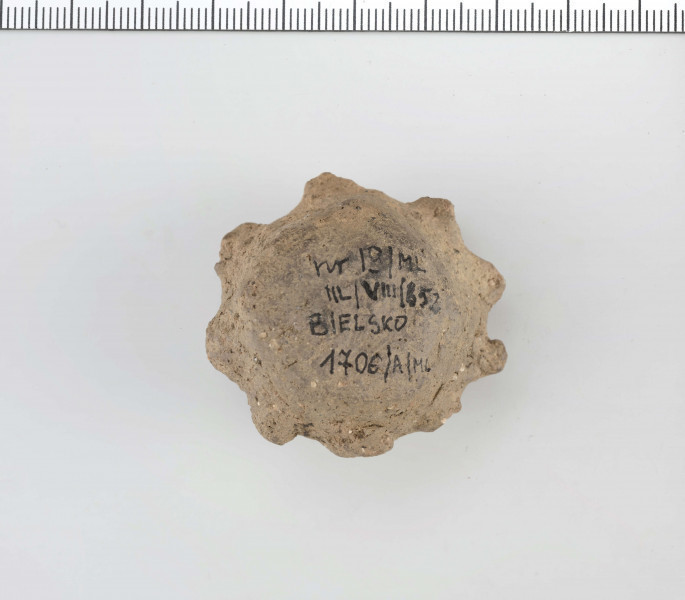 Grzechotka gliniana. Kształt zbliżony do walcowatego. W połowie wysokości ozdobiona 9 guzkami.