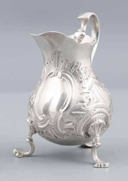 S/Mt/581/ML - Korpus o kształcie gruszkowatym, z wydłużonym wylewem, na trzech nóżkach, ucho profilowane. Krawędź wylewu wycięta faliście, korpus repusowany: na froncie rocaillowy kartusz, po bokach ornamenty wolutowe i kwiatowe.
Na spodzie znaki:
- urząd probierczy w Londynie
- próba Sterling
- oznaczenie roku 