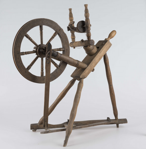 E/16647/ML - Kołowrotek poziomy, drewniany, ozdobnie toczony. Drewno niemalowane. Podstawa to 3 skośnie ustawione nóżki. Dwie z nich osadzone w wąskiej listwie. Górne końce nóżek osadzone w prostokątnej pochyłej grubej desce (11 x 32 x 4 cm). Stanowi ona podstawę do osadzenia koła napędowego i szpuli zwijającej nici. W niej zamocowany uchwyt połączony ze śrubą, która reguluje położenie szpuli. Koło osadzone na metalowej ośce posiada 8 toczonych ozdobnie szprych. Jeden koniec ośki połączony pionową ruchomą listewką z pedałem wprawiającym w ruch kołowrotek. Szpula osadzona również na metalowej ośce.