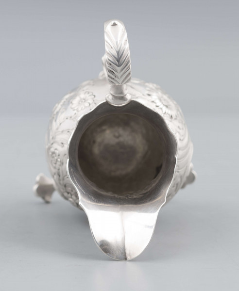 S/Mt/581/ML - Korpus o kształcie gruszkowatym, z wydłużonym wylewem, na trzech nóżkach, ucho profilowane. Krawędź wylewu wycięta faliście, korpus repusowany: na froncie rocaillowy kartusz, po bokach ornamenty wolutowe i kwiatowe.
Na spodzie znaki:
- urząd probierczy w Londynie
- próba Sterling
- oznaczenie roku 