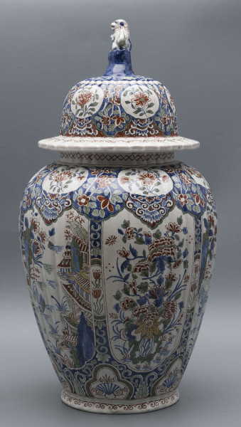 S/CS/546/ML - Wazon owoidalny o niskiej podstawie i niskiej pierścieniowej szyi, powierzchnia drobno kanelowana, pokrywa kopulasta z szerokim kołnierzem, uchwyt w kształcie lwa Fo wspartego prawą łapą na pniu drzewa (?). Dekoracja malowana podszkliwnie w kolorach błękitu, czerwieni, zieleni, żółcieni. W sześciu owalnych, wydłużonych rezerwach na przemian kompozycja kwiatowa z peonią i pejzaż nadrzeczny z architekturą o charakterze orientalnym. U góry - na barkach - sześć owalnych rezerw z kwitnącą gałązką, na dole sześć rezerw trójlistnych z motywem uproszczonej muszli i wolut, na stopie fryz wolutowy, na szyi wąska ukośna kratka. Na pokrywie powtórzona dekoracja z barków, kołnierz biały z fryzem wolutowym analogicznie jak na stopie.
 