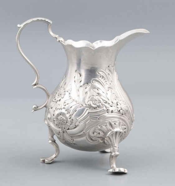 S/Mt/581/ML - Korpus o kształcie gruszkowatym, z wydłużonym wylewem, na trzech nóżkach, ucho profilowane. Krawędź wylewu wycięta faliście, korpus repusowany: na froncie rocaillowy kartusz, po bokach ornamenty wolutowe i kwiatowe.
Na spodzie znaki:
- urząd probierczy w Londynie
- próba Sterling
- oznaczenie roku 