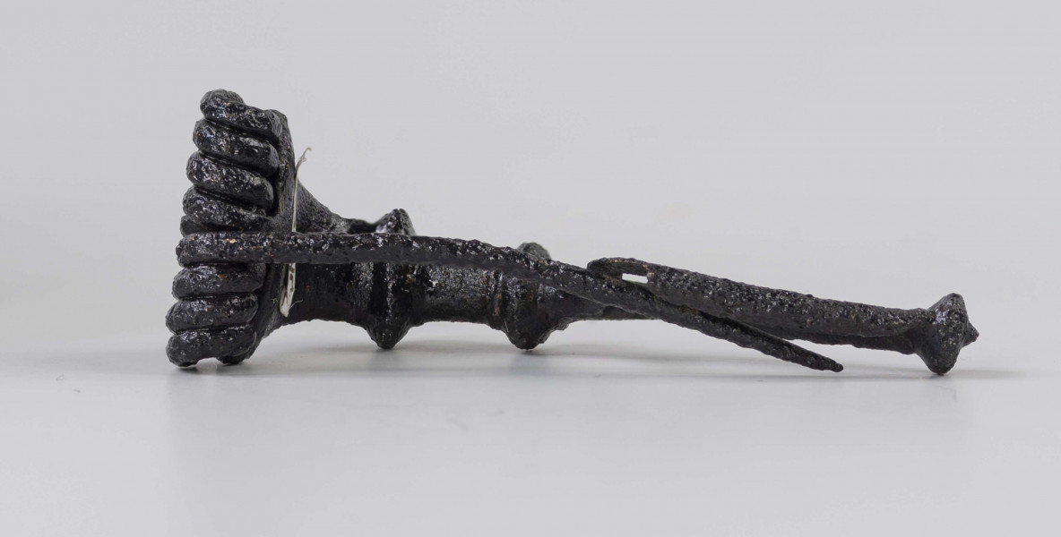 Fibula z brązu o ośmiozwojowej sprężynie i górnej cięciwie. Główka rozszerzająca się ku sprężynie, z dwoma grzebykami na kabłąku i trzecim na końcu nóżki. Typ Almgren 65 ?