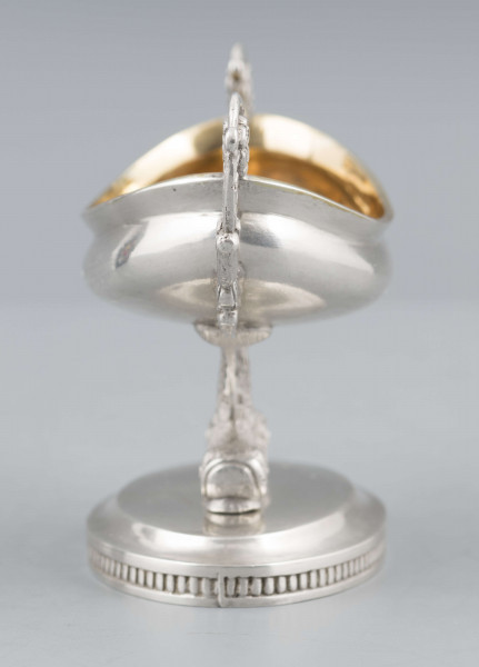 S/Mt/511/ML - Solniczka w formie łódki wspartej na dwóch delfinach, z owalną podstawą, z dwoma uchami z wici roślinnej. Brzeg czarki wywinięty, podstawa lekko podniesiona a jej brzeg zdobiony pionowym karbowaniem. Na spodzie sygnatura:
- imienna 