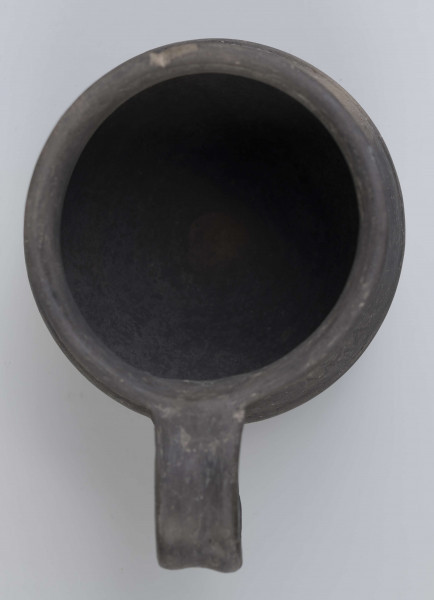 Dno płaskie, wyraźnie wyodrębnione stopką skośnie ściętą ku dołowi; dno wyodrębnione od części przydennej dookolnym wgłębieniem; lekko rozszerzające się ku górze, brzusiec łagodnie zaokraglony, ku górze zwężający się, przechodzący w wysoką, cylindryczną szyjkę; wylew płasko ścięty, rozchylony na zewnątrz; na największej wydętości brzuśca dookolny żłobek; w miejscu przejścia brzuśca w szyję i w połowie szyi dookolny wypukłe listwy; ucho z taśmy środkiem wklęsłej, biegnące od wylewu do załomu brzuśca, szyja zdobiona różnym ornamentem (trzy pasy) przez wygładzenie; powierzchnia gładzona, wyświecona
wymiary dodatkowe: 17,0 cm (obwód); 8,0 cm (śr. dna); 0,3 cm (wys. stopki); 0,5 cm (wys. szyi)