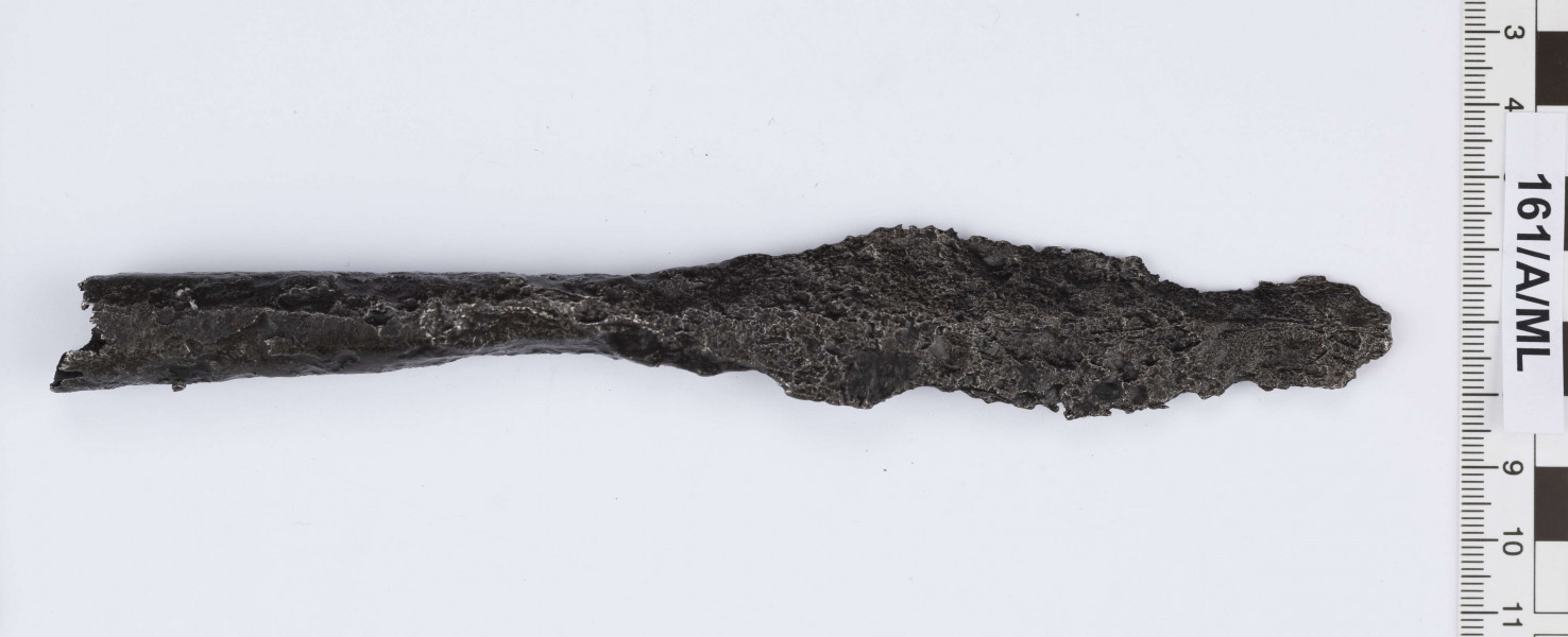 161/A/ML - Żelazny grot oszczepu. Ostrze laurowate, w przekroju soczewkowate z lekko zaznaczonymi żeberkami po obu stronach. Przejście w tuleję bardzo łagodnie wyprofilowane. Tuleja w przekroju nieznacznie spłaszczonego koła, rozszerzająca się ku końcowi. Wewnątrz tulei zachowane resztki drzewca. 
