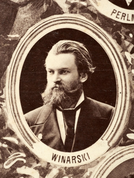 Fotografie w odcieniu sepii umieszczone na tle drzew i roślin, w centralnym miejscu postać kobiety ze sztandarem i aniołkami, wkomponowane widoki budowanej stacji, mostu kolejowego i lokomotywy. Największe zdjęcie w górnej, środkowej części bez podpisu, prawdopodobnie inż. głównej kolei nadwiślańskiej Tadeusz Chrzanowski lub jego następca Walery Titkow. Wśród podobizn pracownicy Biura Głównego Inżyniera: inż. Włodzimierz Stanisławski - pomocnik głównego inżyniera; inż. Feliks Kucharzewski -  pomocnik naczelnika biura; Feliks Kamocki - naczelnik kancelarii; Witold Lanci - naczelnik Wydz. Architektury; dr Wacław Lasocki- służba zdrowia; Władysław Radwan - sprawy zakupu gruntów; inż. Stanisław hr Scipio - projektant mostów kolejowych i jego współpracownicy: inż. Stefan Zieliński, inż. Maurycy Machalski, inż. Feliks Kucharzewski. Fotografia w passe - partout, za szkłem, oprawiona w drewnianą, profilowaną ramę.