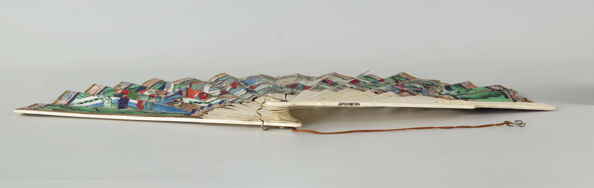 S/R/68/ML - Wachlarz rozkładany. Pokrycie asymetryczne, dwustronne, malowane gwaszem. Twarze postaci wykonane z malowanych, naklejanych, płytek kości słoniowej, ich stroje z malowanych kawałków tkaniny jedwabnej również naklejanych na papier pokrycia. Na wachlarzu przedstawiono sceny rodzajowe w charakterystycznej perspektywie (widziane nieco z góry) w kompozycji kontynuacyjnej, przedstawiają dworzan w towarzystwie wysokiego urzędnika, w scenerii pałacowego ogrodu z pawilonami. Barwne stroje z jedwabiu nawiązują do dworskiej mody i są niezwykle zróżnicowane.   Podkreślone są różnice w formie i detalu stroju. Urzędowe nakrycie głowy, foutou, wyróżnia jedną z przedstawionych postaci, cesarza (?). Stelaż z kości słoniowej, rzeźbiony w motywy roślinne i figuralne, pióra okładzinowe gładkie. Zdobią je pojedyncze, owalne, rzeźbione kompozycje, medaliony ze scenami figuralnymi. Pierścień mosiężny spina stelaż.