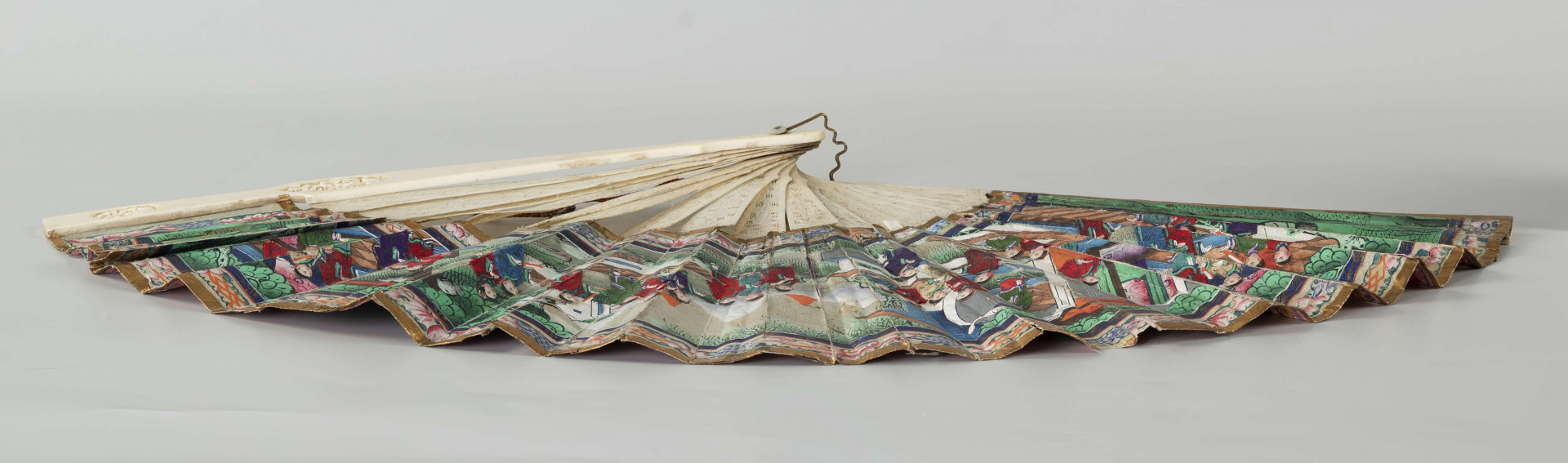 S/R/68/ML - Wachlarz rozkładany. Pokrycie asymetryczne, dwustronne, malowane gwaszem. Twarze postaci wykonane z malowanych, naklejanych, płytek kości słoniowej, ich stroje z malowanych kawałków tkaniny jedwabnej również naklejanych na papier pokrycia. Na wachlarzu przedstawiono sceny rodzajowe w charakterystycznej perspektywie (widziane nieco z góry) w kompozycji kontynuacyjnej, przedstawiają dworzan w towarzystwie wysokiego urzędnika, w scenerii pałacowego ogrodu z pawilonami. Barwne stroje z jedwabiu nawiązują do dworskiej mody i są niezwykle zróżnicowane.   Podkreślone są różnice w formie i detalu stroju. Urzędowe nakrycie głowy, foutou, wyróżnia jedną z przedstawionych postaci, cesarza (?). Stelaż z kości słoniowej, rzeźbiony w motywy roślinne i figuralne, pióra okładzinowe gładkie. Zdobią je pojedyncze, owalne, rzeźbione kompozycje, medaliony ze scenami figuralnymi. Pierścień mosiężny spina stelaż.