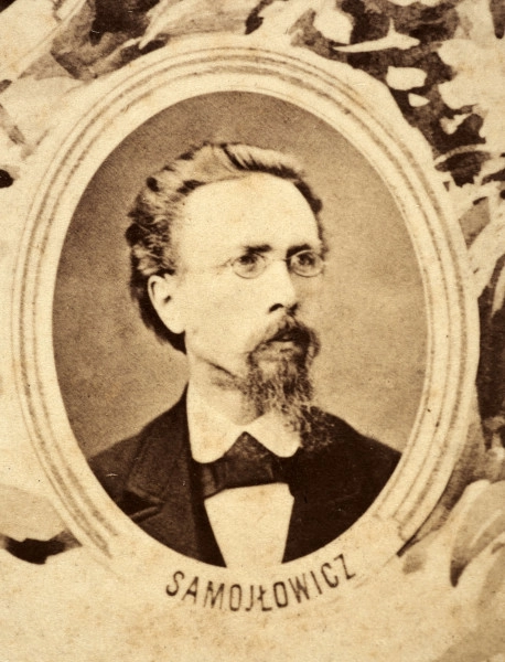 Fotografie w odcieniu sepii umieszczone na tle drzew i roślin, w centralnym miejscu postać kobiety ze sztandarem i aniołkami, wkomponowane widoki budowanej stacji, mostu kolejowego i lokomotywy. Największe zdjęcie w górnej, środkowej części bez podpisu, prawdopodobnie inż. głównej kolei nadwiślańskiej Tadeusz Chrzanowski lub jego następca Walery Titkow. Wśród podobizn pracownicy Biura Głównego Inżyniera: inż. Włodzimierz Stanisławski - pomocnik głównego inżyniera; inż. Feliks Kucharzewski -  pomocnik naczelnika biura; Feliks Kamocki - naczelnik kancelarii; Witold Lanci - naczelnik Wydz. Architektury; dr Wacław Lasocki- służba zdrowia; Władysław Radwan - sprawy zakupu gruntów; inż. Stanisław hr Scipio - projektant mostów kolejowych i jego współpracownicy: inż. Stefan Zieliński, inż. Maurycy Machalski, inż. Feliks Kucharzewski. Fotografia w passe - partout, za szkłem, oprawiona w drewnianą, profilowaną ramę.
