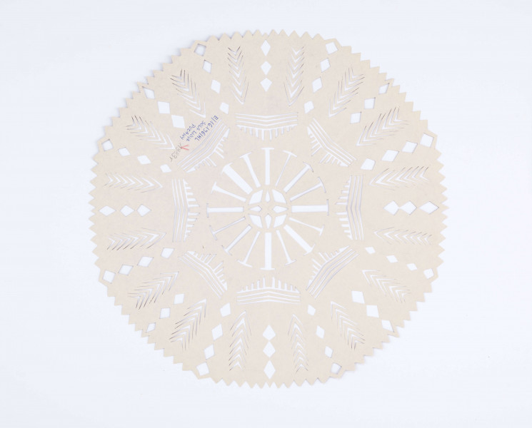 Wycinanka kolista z glansowanego papieru w kolorze brązowym, o ośmiu osiach symetrii. W centrum gwiazda czteroramienna. Na pozostałej powierzchni wycięcia w postaci paseczków pionowych i poziomych, ułożonych grupami. Na otoku wycięcia w postaci rombów i kłosów stylizowanych. 