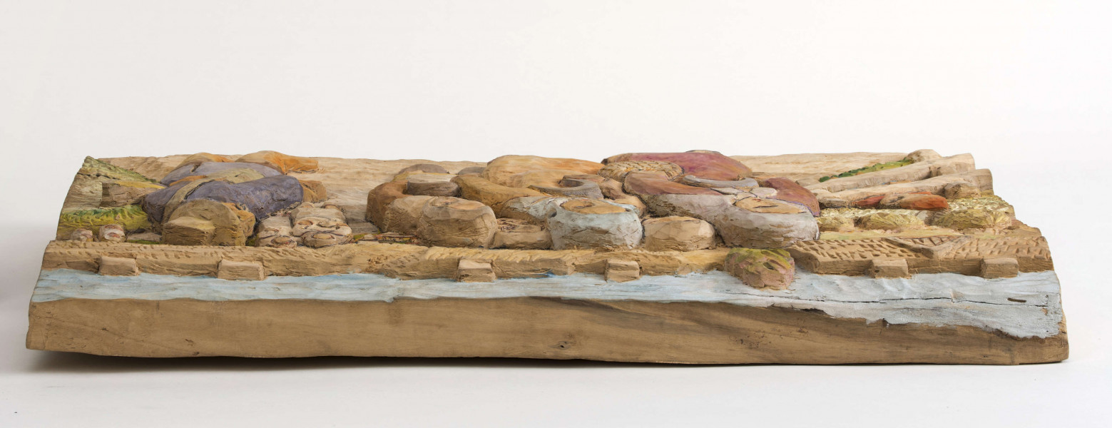 Płaskorzeźba z drewna lipowego, technika strugania, polichromowana przedstawiająca grupę kobiet i ekonoma. Centralnie zakomponowana została grupa kobiet, składająca się z 5 osób, idących drogą (droga niepolichromowana). Sylwetki trzech kobiet w całości, dwóch – widoczne tylko głowy. Kobiety z przodu są w sukienkach sięgających za kolana (kobieta z lewej ma w pasie przewiązany  fartuszek), białych chustkach na głowie i zawiązanych pod brodą, półbutach. Kobieta z prawej, w prawej ręce trzyma sierp, w lewek koszyczek. Kobieta w środku – w prawej ręce trzyma sierp. Kobieta  z lewej – sierp trzyma w lewej ręce. 
Z lewej strony płaskorzeźby zakomponowana postać ekonoma., w fioletowej kurtce przespanej pomarańczowym pasem, z przewieszona przez ramię torbą, w żółtawym kapeluszu z rondem, w brązowych spodniach wpuszczonych w buty z cholewami. Postać przedstawiona z tyłu, głowa z profilu. W prawej ręce, przez łokieć, wysunięty bat. W głębi z prawej strony ekonoma – sylwetki dwóch kobiet en face, z lewej – dwoje dzieci. 
Z prawej strony płaskorzeźby – pole, na którym w głębi widoczne są snopy zboża, z przodu – na polu za ogrodzeniem, postać chłopca w czerwonej szpiczastej czapce, czerwonej bluzie i niebieskich spodniach. W głębi na tle widoczne, z prawej strony,  dworek oraz dalej 3 chaty.