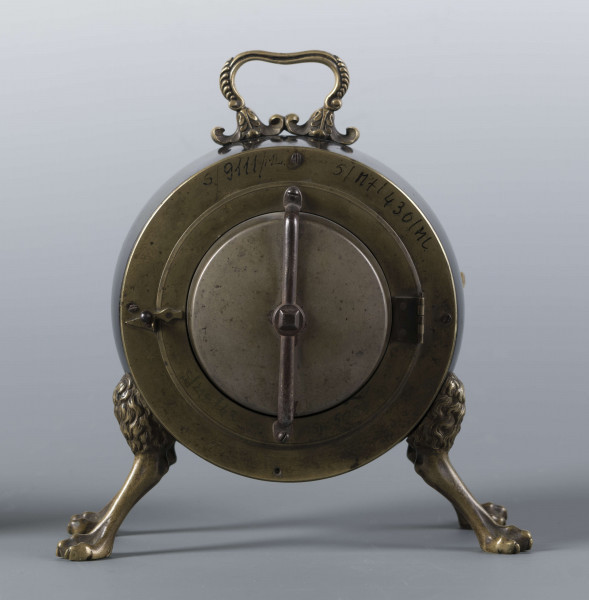 S/Mt/430/ML - Obudowa z brązu w formie bębna leżącego na czterech zwierzęcych łapach, pokrytego czarnym lakierem, z pionowym uchwytem w formie rozciągniętej profilowanej, wolutki. Tarcza zegarowa z mosiądzu, okrągła, moletowana mz malowanymi czarnymi cyframi rzymskimi godzin i oznaczeniem minut; dwie proste wskazówki; osłonieta zamykaną szybką o wypukłym profilu. Zamknięcie z tyłu w postaci okrągłych drzwiczek na zawiasie, z wmontowanym jednym dzwonkiem. Mechanizm mosiężny, o naciągu sprężynowym, z biciem godzin i kwadransów.
Na płycie wewnętrznej mechanizmu grawerowana sygnatura kursywą:
- Jacobus Staigier Lublin
