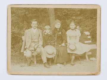 Fotografia przedstawia cztery osoby siedzące na ławce w parku. Od lewej obok siebie siedzą: Juliusz Pol, Jerzy Pol, Zofia Czerwińska - matka Jerzego, Idalia Polówna (rodzina Marka Stanisława Pola, syna W. Pola). Szesnastoletni Juliusz ubrany w jasny garnitur. Sześcioletni Jerzy ubrany w ciemną bluzę, w rękach trzyma duży kapelusz. Zofia w czarnej sukni z parasolką w prawej ręce. Dwunastoletnia Idalia ubrana w jasną sukienkę, w rękach trzyma mały kapelusz. Fotografia naklejona na sztywny kartonik.