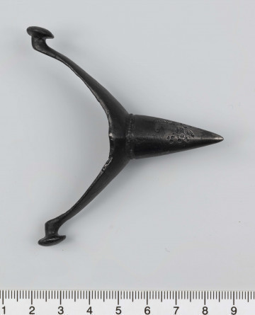 1044/A/ML/1 - Ostroga żelazna z wklęsłym do wewnątrz, łukowatym kabłąkiem. Szeroki przy nasadzie kolca kabłąk zwęża sie stopniowo, przechodząc w wałkowate wygięcia zaczepu, zakończone soczewkowatymi guzkami. Kolec częściowo pusty, ma kształt przegiętego nieznacznie, facetowanego stożka. Przy nasadzie dwie wypiłowane bruzdy z gęsto poprzecznie nacinanym grzbietem powstałym między nimi. Ostroga stanowi element wyposażenia ciałopalnego pochówku złożonego prawdopodobnie w popielnicy. Odkrycia dokonano w 1959 roku przypadkowo w czasie prac rolnych. Oprócz trzech grotów, pochówkowi wojownika towarzyszyły: żelazne umbo, dwie ostrogi, tok brązowy (prawdopodobnie okucie drzewca oszczepu) a także żelazny miecz z miedziana inkrustacją wyobrażającą rzymskich bogów. Pochowany na terenie obecnej wsi Podlodów wojownik należał do elity wojskowej przedstawicieli kultury przeworskiej.
Wymiary dodatkowe: 1,6 cm (podstawa kolca); 1,0 cm (śr. guzków); 3,2 cm (szer. kabłąka przy nasadzie kolca); 0,5 cm (szer. kabłaka przy zaczepach)