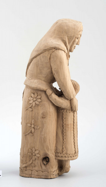 Rzeźba w drewnie lipowym, niepolichromowana, przedstawiająca postać kobiety nachylonej nad dzieckiem, stojącym przy kolanach. Kobieta w chustce na głowie zawiązanej pod brodą, o twarzy trójkątnej, dużych oczach, wąskich ustach. Ubrana w bluzkę z długimi rękawami i serdak z zaznaczoną baskinką , w długiej spódnicy pokrytej stylizowanymi wielopłatkowymi kwiatami na gałązce. U dołu biegnie pasek w formie falistej linii. Kobieta obejmuje rękami dziecko, zwrócone do niej twarzą. Dziecko z włosami sięgającymi do szyi, zaznaczonymi rowkowanymi nacięciami – uczesane z przedziałkiem  pośrodku. W długiej sukience, ozdobionej falistymi liniami poziomymi u dołu i góry, pionowymi pośrodku. 