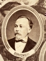 Fotografie w odcieniu sepii umieszczone na tle drzew i roślin, w centralnym miejscu postać kobiety ze sztandarem i aniołkami, wkomponowane widoki budowanej stacji, mostu kolejowego i lokomotywy. Największe zdjęcie w górnej, środkowej części bez podpisu, prawdopodobnie inż. głównej kolei nadwiślańskiej Tadeusz Chrzanowski lub jego następca Walery Titkow. Wśród podobizn pracownicy Biura Głównego Inżyniera: inż. Włodzimierz Stanisławski - pomocnik głównego inżyniera; inż. Feliks Kucharzewski -  pomocnik naczelnika biura; Feliks Kamocki - naczelnik kancelarii; Witold Lanci - naczelnik Wydz. Architektury; dr Wacław Lasocki- służba zdrowia; Władysław Radwan - sprawy zakupu gruntów; inż. Stanisław hr Scipio - projektant mostów kolejowych i jego współpracownicy: inż. Stefan Zieliński, inż. Maurycy Machalski, inż. Feliks Kucharzewski. Fotografia w passe - partout, za szkłem, oprawiona w drewnianą, profilowaną ramę.