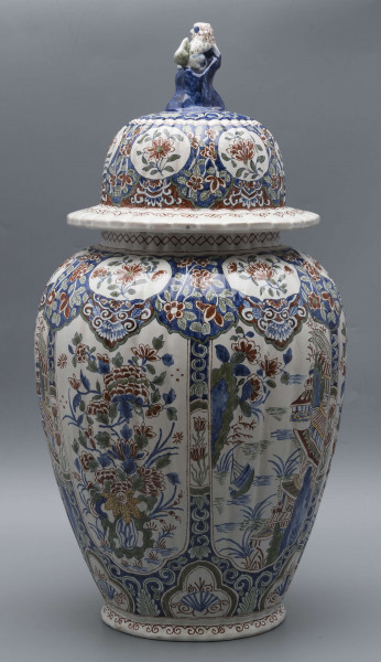 S/CS/546/ML - Wazon owoidalny o niskiej podstawie i niskiej pierścieniowej szyi, powierzchnia drobno kanelowana, pokrywa kopulasta z szerokim kołnierzem, uchwyt w kształcie lwa Fo wspartego prawą łapą na pniu drzewa (?). Dekoracja malowana podszkliwnie w kolorach błękitu, czerwieni, zieleni, żółcieni. W sześciu owalnych, wydłużonych rezerwach na przemian kompozycja kwiatowa z peonią i pejzaż nadrzeczny z architekturą o charakterze orientalnym. U góry - na barkach - sześć owalnych rezerw z kwitnącą gałązką, na dole sześć rezerw trójlistnych z motywem uproszczonej muszli i wolut, na stopie fryz wolutowy, na szyi wąska ukośna kratka. Na pokrywie powtórzona dekoracja z barków, kołnierz biały z fryzem wolutowym analogicznie jak na stopie.
 