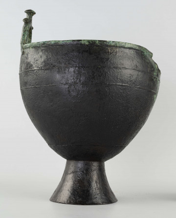 709/A/ML - ponad lekko wygiętą na zewnątrz krawędź wznosi się kabłąkowaty uchwyt ozdobiony trzema gwoździowatymi trzpieniami; podobny uchwyt prawdopodobnie był umieszczony symetrycznie na przeciwległej, wyłamanej części krawędzi; wzdłuż największej wydętości brzuśca znajdują się dwie równoległe, wypukłe listewki, prawdopodobnie imitujące sznur; w blasze kotła widoczne ślady napraw uszkodzeń powstałych w czasie użytkowania; patyna szlachetna pokrywa kocioł na prawie całej powierzchni