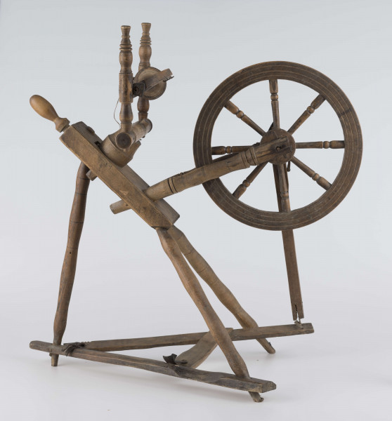 E/16647/ML - Kołowrotek poziomy, drewniany, ozdobnie toczony. Drewno niemalowane. Podstawa to 3 skośnie ustawione nóżki. Dwie z nich osadzone w wąskiej listwie. Górne końce nóżek osadzone w prostokątnej pochyłej grubej desce (11 x 32 x 4 cm). Stanowi ona podstawę do osadzenia koła napędowego i szpuli zwijającej nici. W niej zamocowany uchwyt połączony ze śrubą, która reguluje położenie szpuli. Koło osadzone na metalowej ośce posiada 8 toczonych ozdobnie szprych. Jeden koniec ośki połączony pionową ruchomą listewką z pedałem wprawiającym w ruch kołowrotek. Szpula osadzona również na metalowej ośce.