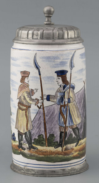 S/CS/64/ML - Korpus cylindryczny z uchem w kształcie litery „C”, pokrywka cynowa, płaska z profilowanym brzegiem i kulistą sterczyną  na zawiasie umocowanym do ucha; profilowana cynowa obręcz otacza dolną krawędź. Pokryty białym szkliwem z wielobarwną dekoracją malowaną skomponowaną przeciwlegle do ucha. Przedstawia ona w uproszczony sposób scenę w obozie  wojskowym: dwaj uzbrojeni kosynierzy stoją na wprost siebie, za nimi widoczny namiot a wokół zielone zarośla i drzewa. Niebo zaznaczone błękitnymi plamami, w tym samym kolorze malowane paski obiegają krawędzie naczynia i zdobią ucho. Tematyka przedstawienia ma wyraźnie patriotyczny charakter nawiązując do powstania kościuszkowskiego.

