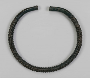 1395/A/ML/2 - Naszyjnik brązowy wykonany z pręta lanego, pokrytego zieloną patyną. Całość spiralnie skręcona; końcówki płasko zaklepane, nieskręcane jedynie ozdobione kilkoma żłobkami nacietymi na zewnętrznej stronie naszyjnika