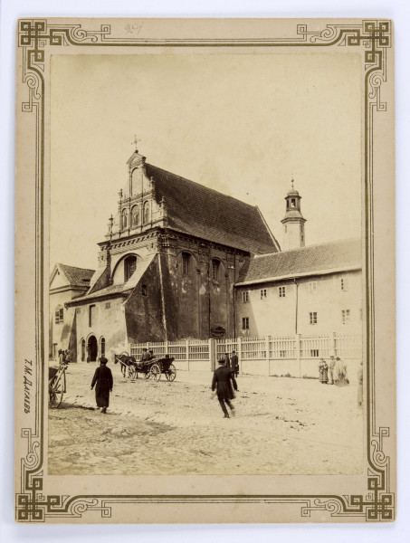 Kościół i klasztor karmelitów bosych przy ulicy Świętoduskiej w Lublinie. Widok zabudowań od strony południowo-zachodniej. Świątynia pod wezwaniem św. Józefa Oblubieńca Najświętszej Marii Panny. Na pierwszym planie ulica brukowana „kocim łbem”. Widocznych kilkoro przechodniów. Pośrodku dorożka zaprzężona do jednego konia. Po lewej stronie widać koło od drugiej z dorożek. Teren przyklasztorny ogrodzony parkanem z przęsłami oddzielonymi słupkami. Budynek klasztoru dwupiętrowy, przylegający do kościoła od strony południowej. Ponad dachem klasztornym widoczna wieżyczka. Bryła świątyni w typie tzw. renesansu lubelskiego z dwuspadowym dachem krytym dachówką. Od strony klasztoru przedzielone pilastrem dwie arkadowe wnęki z oknami u góry. Poniżej jednej z wnęk widoczne małe zadaszenie. Wejście do kościoła wprost z ulicy przez murowaną kruchtę z jednospadowym dachem krytym blachą. Po lewej stronie kruchty przypora wychodząca na chodnik. Pośrodku łukowato zwieńczone wejście główne z przyległymi symetrycznie po obu stronach łukowatymi wnękami. Nad kruchtą, w ścianie frontowej świątyni, w łukowatej niszy widoczne okno. Wyżej, nad fryzem, trójkątny szczyt. W jego trzech łukowatych niszach polichromia z wizerunkami patronów zgromadzenia oraz Matki Bożej Szkaplerznej. Po lewej budynek dawnego domu kapelana.

Fotografia sepiowana, naklejona na tekturę, otoczona ozdobną podwójną ramką w kolorze złotym. Na rogach bogaty ornament geometryczny. Wzdłuż lewej krawędzi nazwisko autora fotografii w języku rosyjskim. Na rewersie w górnym polu napis informacyjny ołówkiem.
