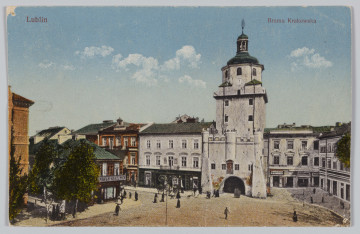 ML/H/3980 - Widok na Bramę Krakowską od strony Placu Łokietka. Budynek Bramy otynkowany, elementy pokrycia dachowego zielone. Kamienice w bezpośrednim sąsiedztwie bramy jasnoszare. Kamienice w lewej części pocztówki ceglasto czerwone, z zielonymi dachami oraz drzewa. Na ulicy sylwetki przechodniów. Niebo jasne, z delikatnymi obłokami.
Na odwrociu nazwa i adres wydawcy.