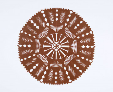 Wycinanka kolista z glansowanego papieru w kolorze brązowym, o ośmiu osiach symetrii. W centrum gwiazda czteroramienna. Na pozostałej powierzchni wycięcia w postaci paseczków pionowych i poziomych, ułożonych grupami. Na otoku wycięcia w postaci rombów i kłosów stylizowanych. 