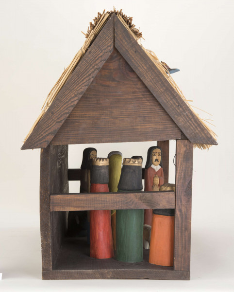 Szopka kolędnicza. Dach dwuspadowy. Na poszyciu dachu figurki trzech drewnianych kolorowych ptaszków. W szopce znajduje się 9 figurek drewnianych przedstawiających postaci ludzkie i żłóbek oraz figurki: osła, wołu i baranka. Pośrodku szopki stoi żłóbek z Dzieciątkiem, po lewej stronie postać Matki Boskiej (wys. 22 cm), po prawej – postać św. Józefa (wys. 22 cm). Za żłóbkiem z tyłu postać Anioła (wys. 21 cm). Przed żłóbkiem figurka przedstawiająca baranka. Z lewej strony wzdłuż ściany figurki trzech króli. Pierwszy król (wys. 16 cm) – murzyn, trzyma w rękach złotą kulę, drugi (wys. 21,5 cm) – złoty domek, trzeci (wys. 22 cm) – złotą księgę. Z prawej strony wzdłuż ściany znajdują się: mężczyzna (wys. 23 cm) w lewej ręce trzymający laskę, a w prawej worek, kobieta (wys. 21 cm) z kurą w rękach oraz – pomiędzy figurkami wołu i osiołka, postać mężczyzny grającego na trąbce. 
Figurki z drewna lipowego, polichromowane.