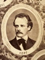 Fotografie w odcieniu sepii umieszczone na tle drzew i roślin, w centralnym miejscu postać kobiety ze sztandarem i aniołkami, wkomponowane widoki budowanej stacji, mostu kolejowego i lokomotywy. Największe zdjęcie w górnej, środkowej części bez podpisu, prawdopodobnie inż. głównej kolei nadwiślańskiej Tadeusz Chrzanowski lub jego następca Walery Titkow. Wśród podobizn pracownicy Biura Głównego Inżyniera: inż. Włodzimierz Stanisławski - pomocnik głównego inżyniera; inż. Feliks Kucharzewski -  pomocnik naczelnika biura; Feliks Kamocki - naczelnik kancelarii; Witold Lanci - naczelnik Wydz. Architektury; dr Wacław Lasocki- służba zdrowia; Władysław Radwan - sprawy zakupu gruntów; inż. Stanisław hr Scipio - projektant mostów kolejowych i jego współpracownicy: inż. Stefan Zieliński, inż. Maurycy Machalski, inż. Feliks Kucharzewski. Fotografia w passe - partout, za szkłem, oprawiona w drewnianą, profilowaną ramę.